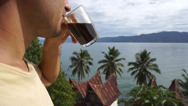 Male traveler drinking coffee and looking at Toba lake from Samosir island