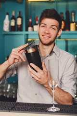 Young handsome barman in bar shaking and mixing alcohol cocktail
