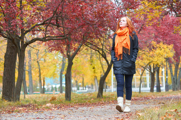 girl walk on pathway in city park with red trees, fall season