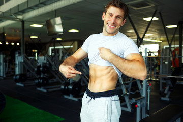 Fototapeta na wymiar Athletic man showing abdominal muscles in gym