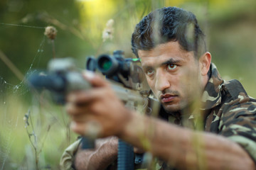 Man of Arab nationality in camouflage with a gun aiming at a tar