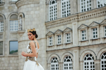 Model with a tender face and crown on her dark hair stands in th