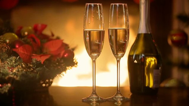 Closeup of two champagne flutes on dinner table at dark room with burning fireplace