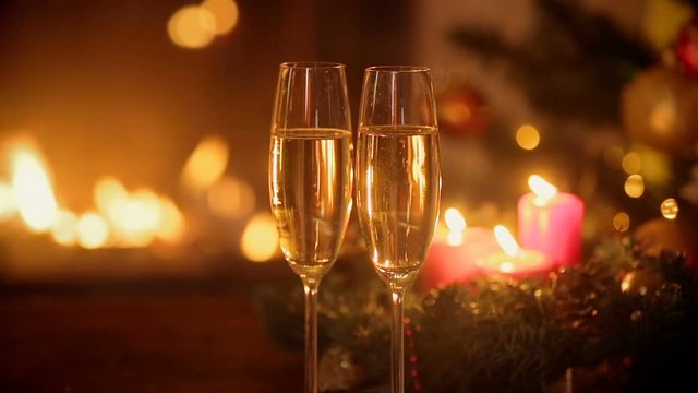 Closeup of two glasses of fizzy champagne in front of burning fireplace. Decorated Christmas tree and burning candles on background.