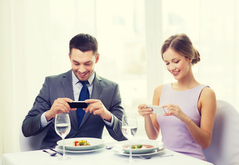 smiling couple with appetizers and smartphones