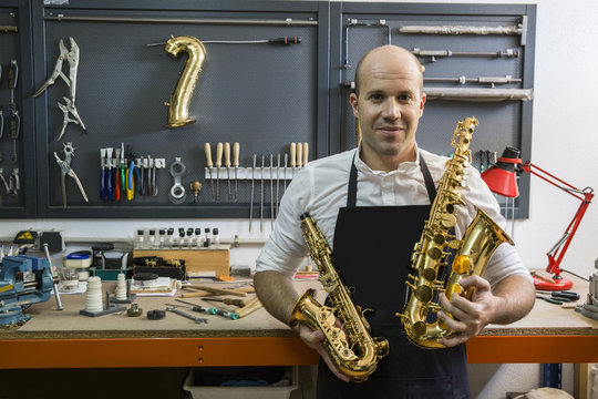 Portrait of an instrument maker holding two saxophones in his workshop