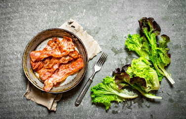 Fried bacon and greens. On stone background.