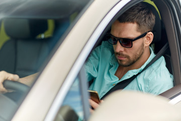 man in sunglasses driving car with smartphone