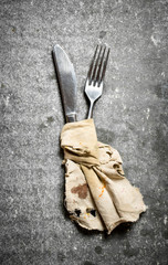Knife and fork wrapped in old cloth. On stone background.