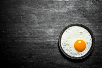 Fried egg in a frying pan. On black wooden background.
