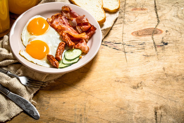 Orange juice with fried eggs, bacon, and slices of bread.