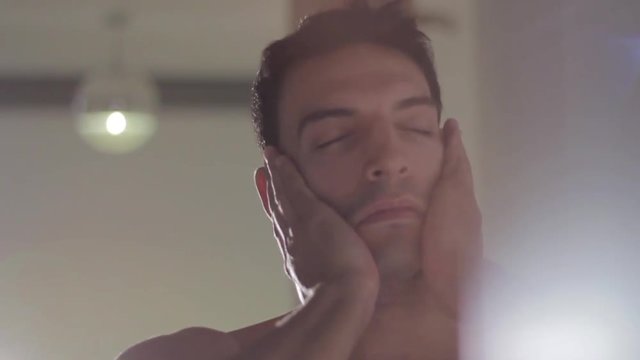 Handsome sexy young dark haired man stretching out naked from the waist up, slo-mo, close-up, tilting. 