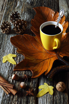 Cup of coffee on wooden maple leaf, nuts and autumn leaves
