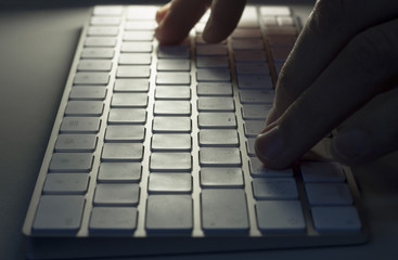 Male hands typing on white computer keyboard, close-up, in the dark