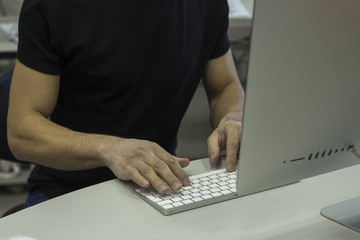 Young man in a black T-shirt working with computer, man's hands on keyboard computer
