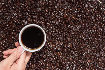 Hand holding a cup of black coffee and roasted coffee beans. Vie