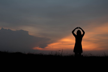 silhouette of woman heart shape making of hands against at sunse