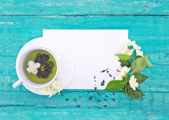 Cup of green tea with jasmine flowers on turquoise rustic wooden