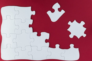 Incomplete white plain jigsaw puzzle on red background.
