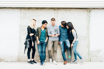 Group of young beautiful multiethnic woman and man friends leaning against a wall outdoor in the city using smart phone - technology, social network, friendship concept