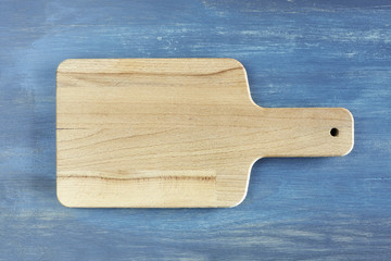 Empty wooden cutting board on rustic blue table, background with space for text, top view.