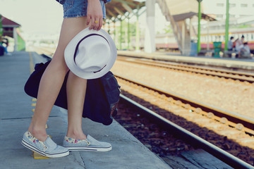 beautiful woman carrying her bag and hat waiting for a train at a railway station,vacation concept