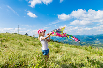 4-5 years girl holding a kite against the backdrop of beautiful mountains and green landscapes