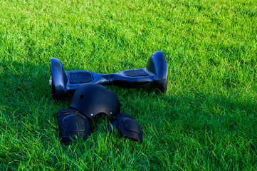 Black gyroscooter with helmet and knee pads on the grass in park.