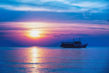 Obraz premium Tropical colorful dramatic sunset with cloudy sky and silhouette of the ship on the horizon. Evening calm on the Gulf of Thailand. Bright afterglow.