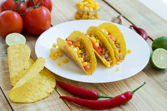 Baked taco shells with chicken mince, tomato and corn and served on a white plate. Ingredients for cooking of traditional mexican tacos
