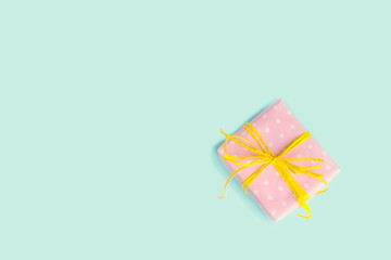 Top view of a gift box wrapped in pink dotted paper and tied yellow bow over light blue background. Vintage effect.