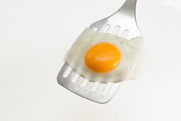 Fried egg on the spatula, ready to be served. White background.