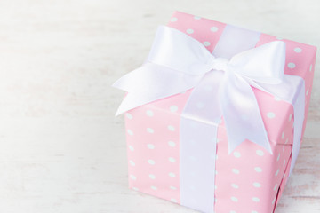 Gift box wrapped in pink dotted paper and tied satin bow over a white wood background.