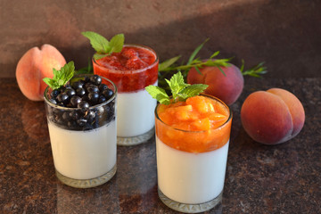 White yogurt with fresh peach and apricot puree, strawberry and black currant, decorated with melissa. Refreshing summer breakfast - 3 different flavors. Cold dessert in glass cups. Selective focus.