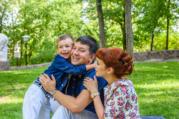 Fototapeta na wymiar Family: Mom, dad and son sitting on the grass in the park