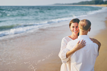 Love and romance. Honeymoon on the sea shore. Beautiful loving couple in white cloth embracing on the beach.