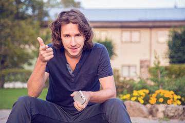 Young, happy man resting outdoor in the evening, holding mobile phone after good telephone conversation and he thinks that in his life everything it's ok.