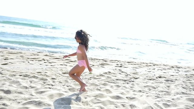 Slow motion of a cute little girl in swimsuit playing at the sea beach