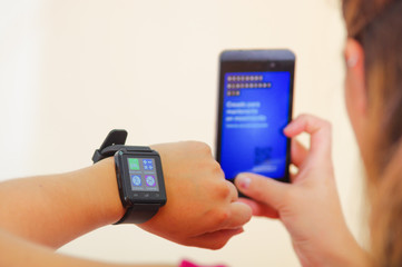 Woman wearing smart watch, holding mobile in other hand, white studio background