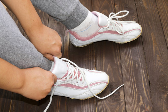 Tying Shoe laces girl sitting on the wooden floor. White sneakers on a dark wooden background.Side view.Fitness , sports.