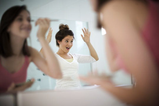 Two teenage girls getting ready in front of a bathroom mirror.