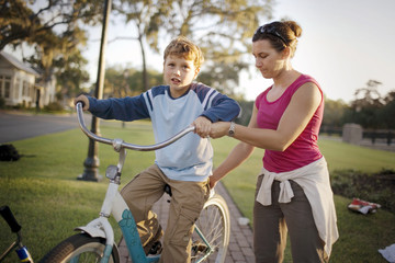 Mid-adult woman helping her son balance while he rides a bicycle.