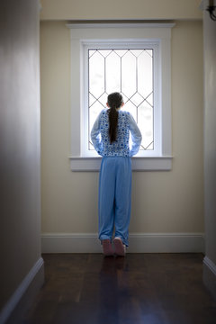 Teenage girl in pyjamas looking out a window.