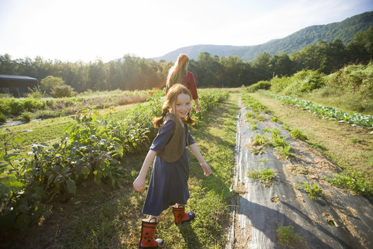 Portrait of a young girl walking with her mid-adult mother through a vegetable field.