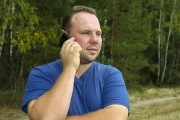 Young man talking on mobile phone in nature, green background. Communication without borders and outside the city.The unshaven man.