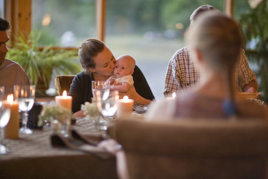 Woman surrounded by family at dinner table kissing baby
