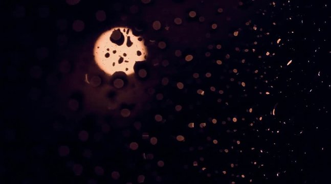 Abstract night city light over wet window with shining rain drops. Movement of the glass, smoth change of depth of field. Time lapse
