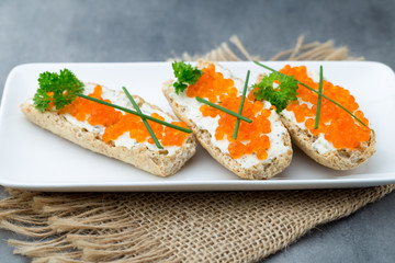Red caviar on bread on white plate.
