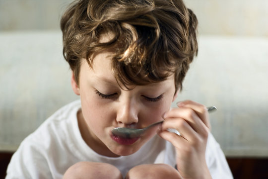 View of a boy sipping a liquid from a spoon.