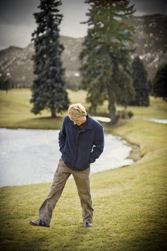 Mid-adult man walking with his hands in his pockets around a golf course.
